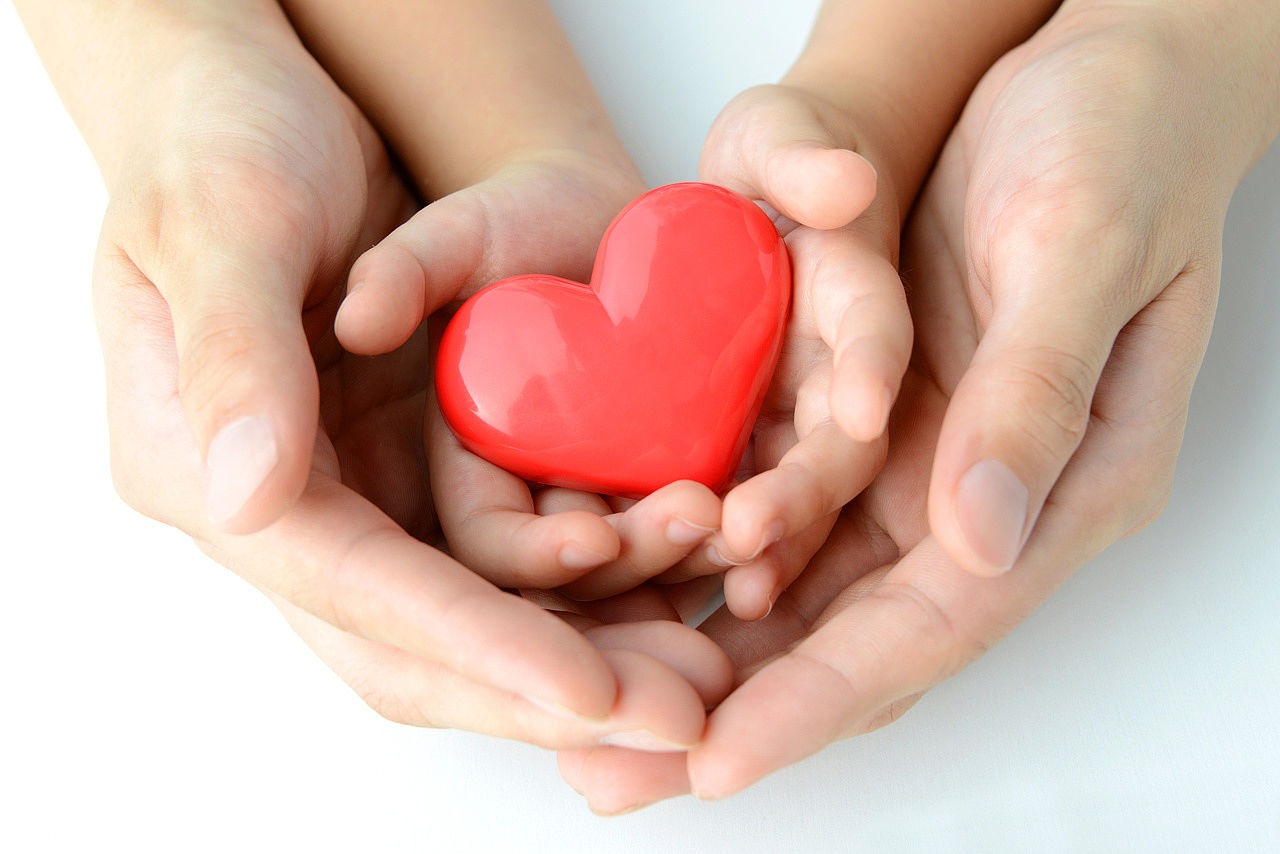 An adult and a child hold a heart in their hands.
